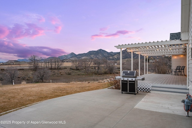 patio terrace at dusk featuring a grill, a deck with mountain view, and a pergola