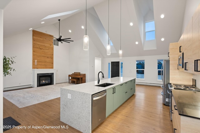 kitchen with a sink, an island with sink, appliances with stainless steel finishes, a glass covered fireplace, and a baseboard radiator