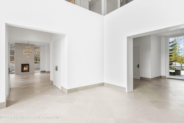 401 Eagle Park Dr, Aspen, CO 81611 - spare room featuring baseboards, light tile patterned floors, a chandelier, a towering ceiling, and a lit fireplace