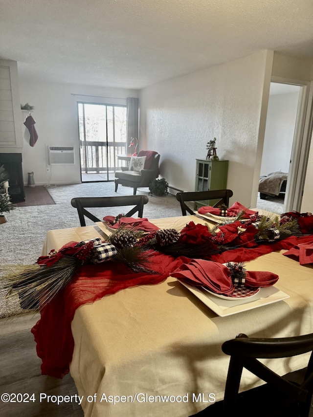 living room with baseboard heating, a wall mounted AC, a textured ceiling, a fireplace, and carpet