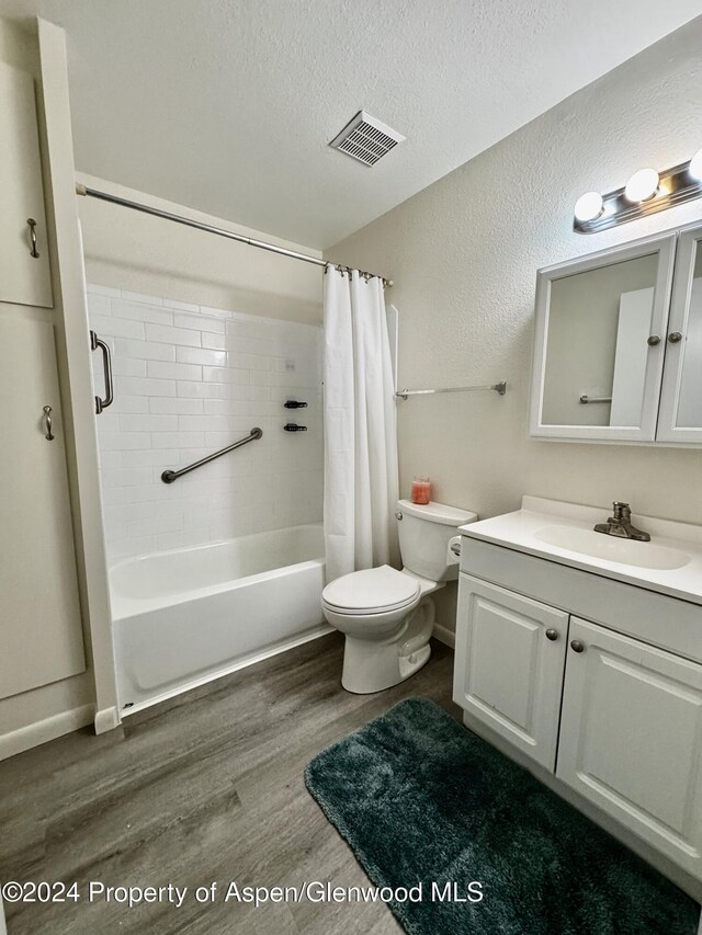 full bathroom with shower / bath combination with curtain, vanity, a textured ceiling, hardwood / wood-style floors, and toilet