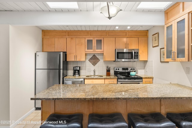 kitchen with light tile patterned floors, a sink, decorative backsplash, a kitchen bar, and appliances with stainless steel finishes