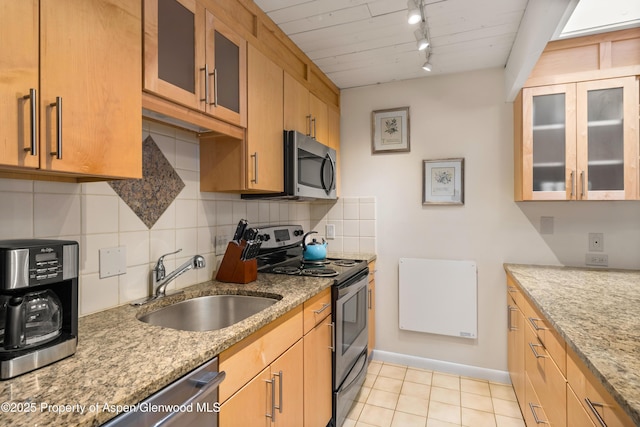 kitchen with light stone counters, a sink, stainless steel appliances, rail lighting, and backsplash