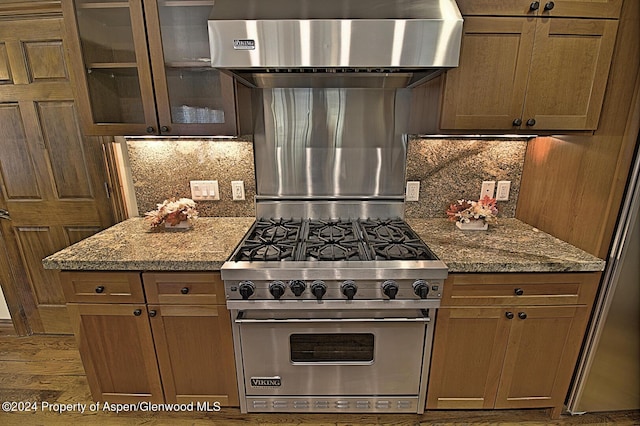 kitchen featuring decorative backsplash, light stone countertops, wall chimney exhaust hood, designer stove, and hardwood / wood-style floors