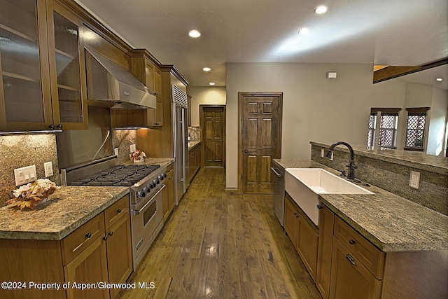 kitchen with high quality appliances, wall chimney range hood, sink, hardwood / wood-style flooring, and tasteful backsplash