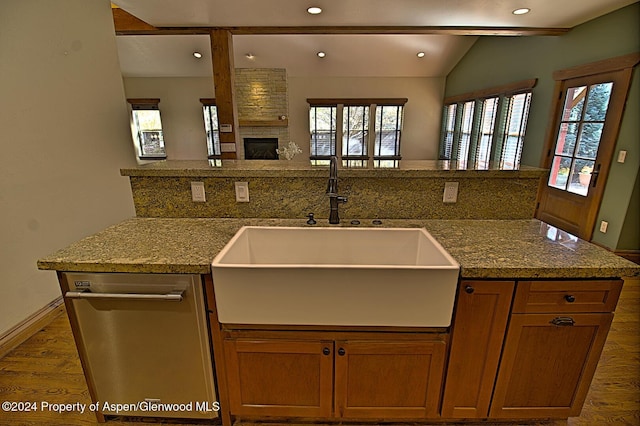 kitchen featuring light stone countertops, sink, stainless steel dishwasher, a fireplace, and hardwood / wood-style flooring