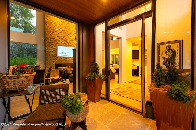 interior space featuring a stone fireplace, floor to ceiling windows, and wooden ceiling