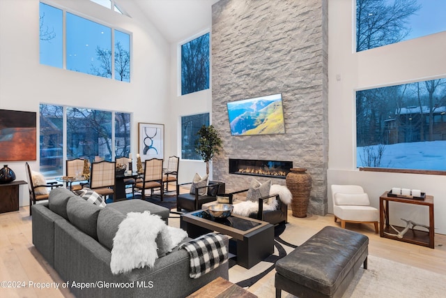 living room with light wood-type flooring, high vaulted ceiling, and a stone fireplace