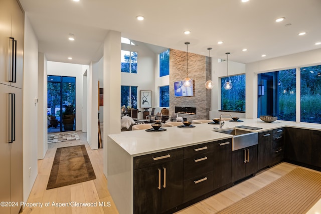 kitchen with a large fireplace, light hardwood / wood-style flooring, kitchen peninsula, decorative light fixtures, and dark brown cabinets