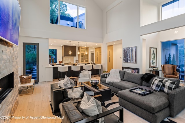 living room with a tiled fireplace, light hardwood / wood-style flooring, and a high ceiling