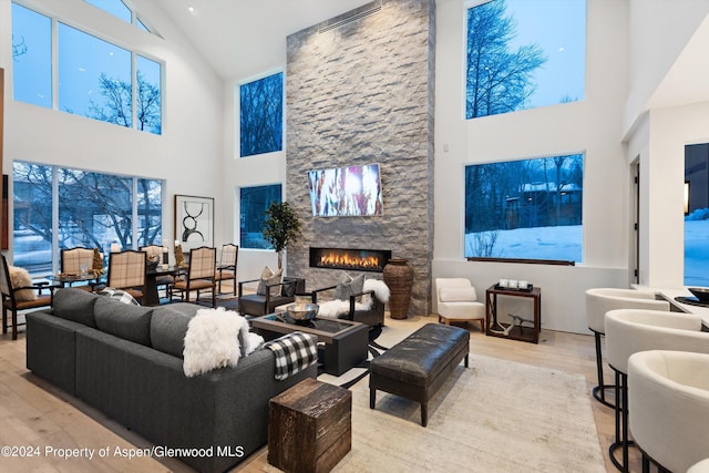 living room with high vaulted ceiling, a stone fireplace, and light hardwood / wood-style floors