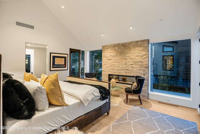 bedroom featuring a stone fireplace, light hardwood / wood-style flooring, and high vaulted ceiling