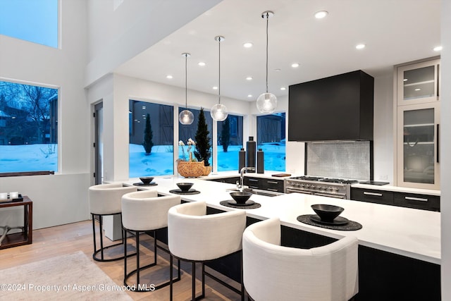 kitchen with light wood-type flooring, extractor fan, sink, high end stainless steel range, and hanging light fixtures