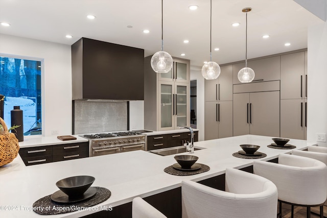 kitchen with a kitchen bar, high end stove, wall chimney range hood, sink, and pendant lighting