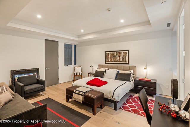 bedroom with a raised ceiling and light wood-type flooring