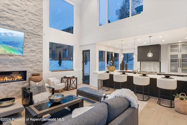 living room with a stone fireplace, a high ceiling, and light wood-type flooring