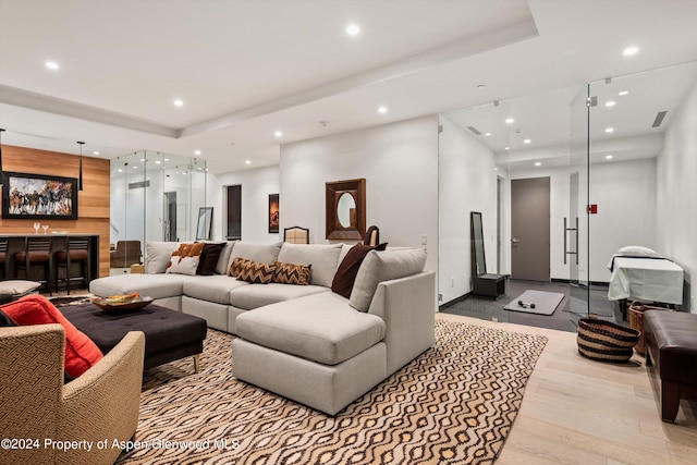 living room with a raised ceiling, light wood-type flooring, and bar