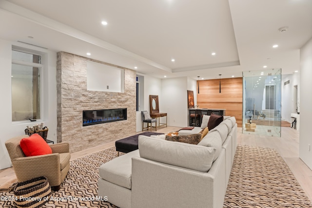 living room with a raised ceiling, light hardwood / wood-style floors, and a stone fireplace