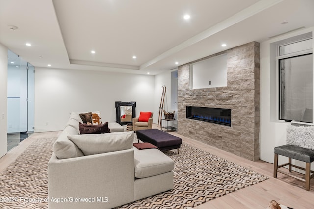 living room with a tray ceiling, a stone fireplace, and light wood-type flooring