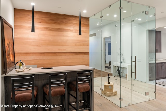 bar with dark brown cabinetry, light wood-type flooring, and wooden walls