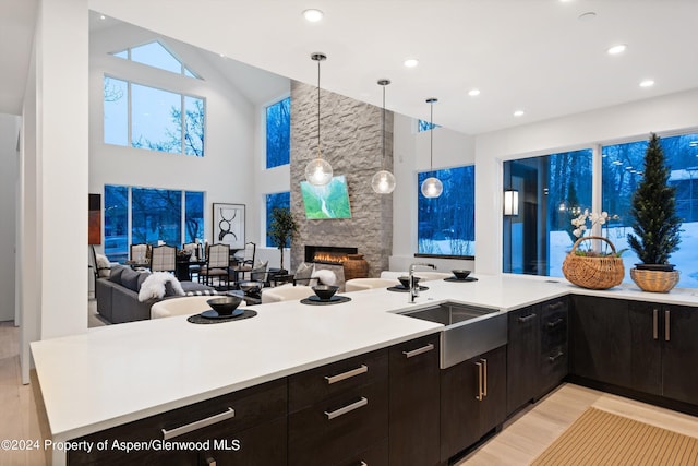 kitchen featuring a stone fireplace, sink, decorative light fixtures, dark brown cabinets, and kitchen peninsula