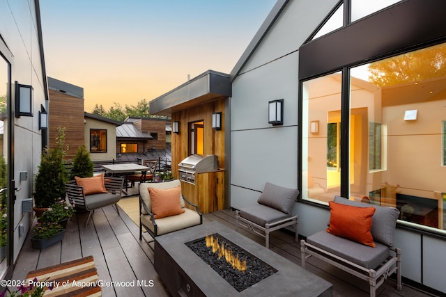 deck at dusk with an outdoor kitchen, area for grilling, and an outdoor fire pit