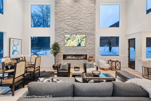 living room with a high ceiling, a stone fireplace, and wood-type flooring