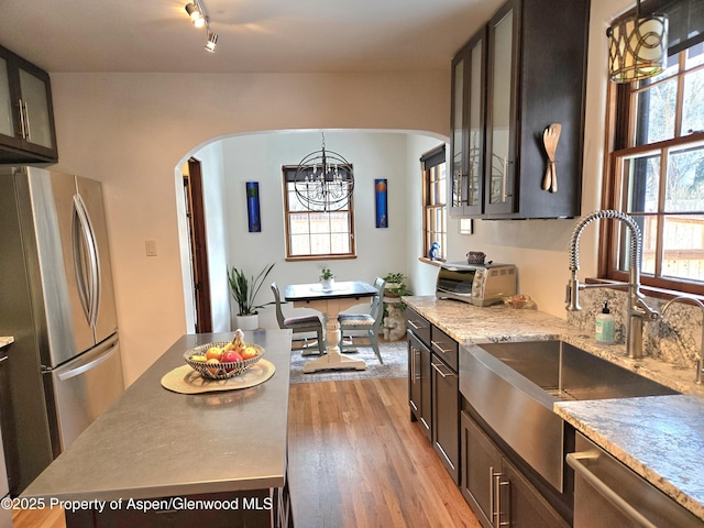 kitchen featuring dark brown cabinetry, sink, light hardwood / wood-style flooring, pendant lighting, and stainless steel appliances