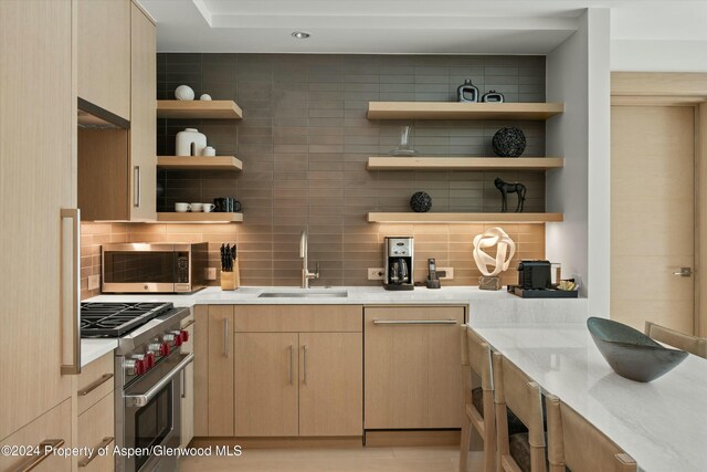 bar featuring light stone countertops, sink, decorative backsplash, light brown cabinetry, and appliances with stainless steel finishes