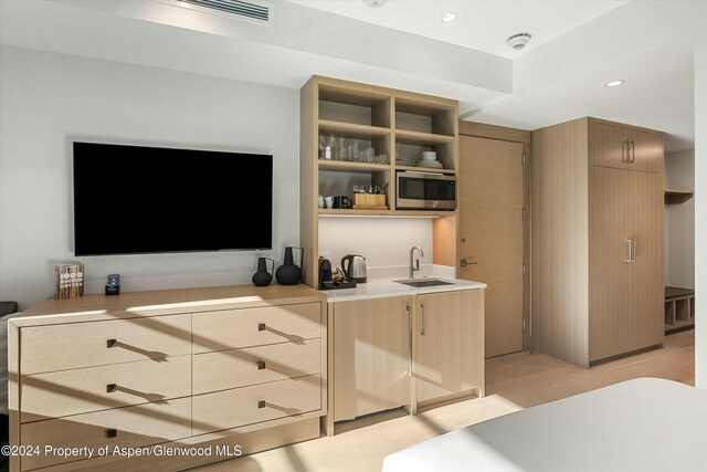 kitchen with light brown cabinetry, stainless steel microwave, and sink