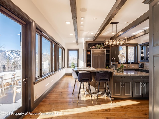 bar with light stone countertops, decorative light fixtures, beamed ceiling, a mountain view, and plenty of natural light