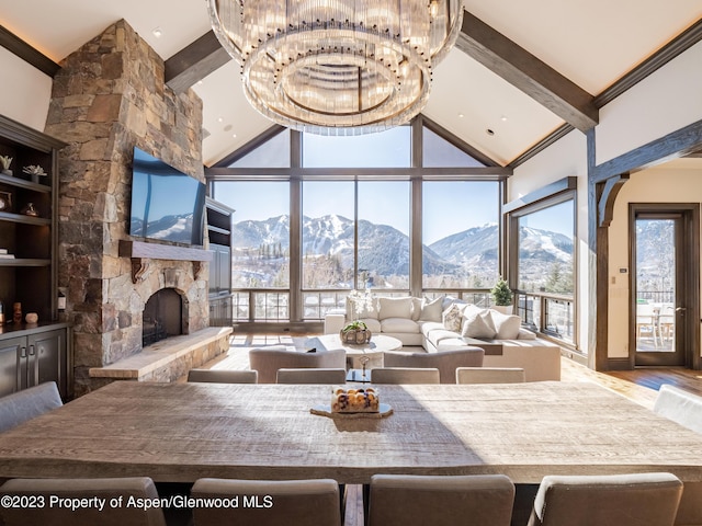 living room featuring beamed ceiling, a healthy amount of sunlight, a stone fireplace, and a chandelier