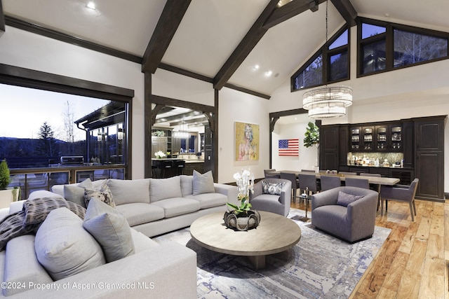 living room featuring light wood-type flooring, high vaulted ceiling, an inviting chandelier, beamed ceiling, and bar