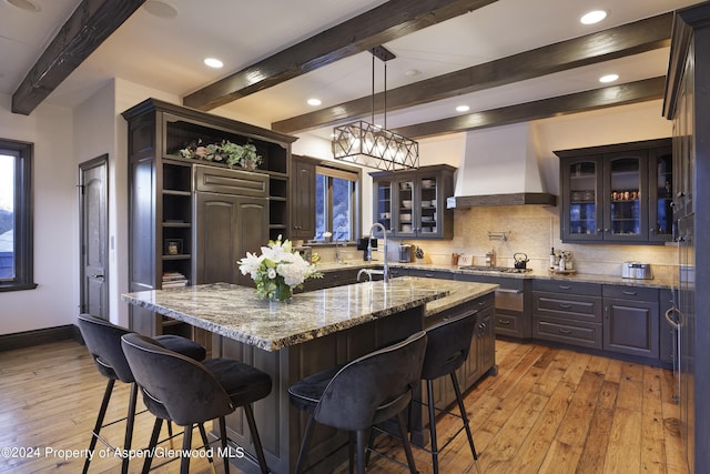 kitchen with custom range hood, tasteful backsplash, light stone counters, and light hardwood / wood-style flooring