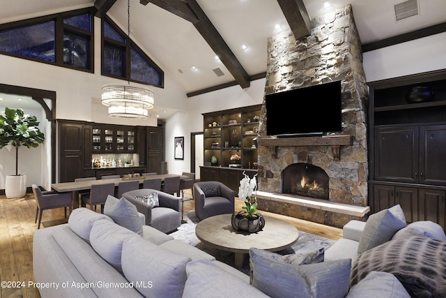 living room with light wood-type flooring, high vaulted ceiling, beamed ceiling, a chandelier, and a stone fireplace