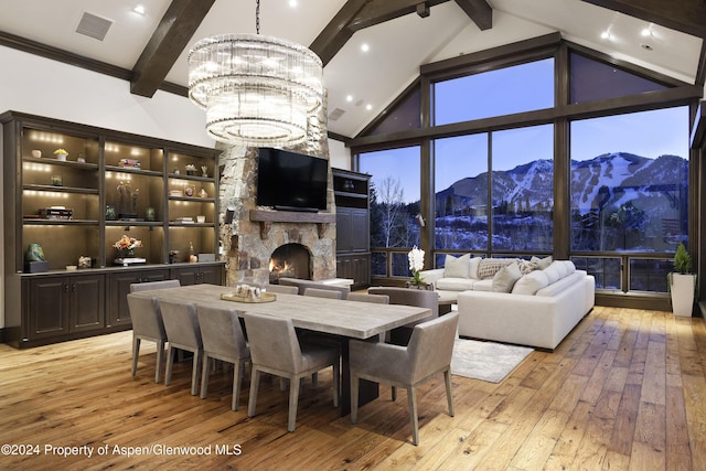 dining space featuring light wood-type flooring, a fireplace, high vaulted ceiling, beamed ceiling, and a chandelier