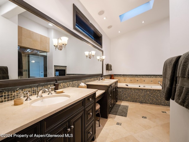 bathroom featuring a skylight, tile patterned floors, vanity, an inviting chandelier, and tiled bath