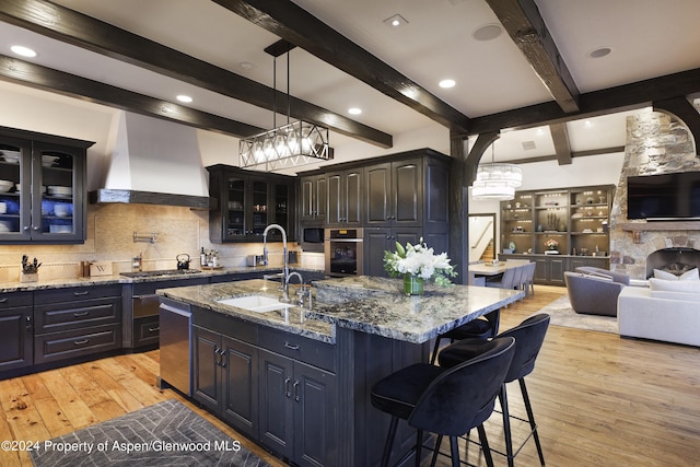 kitchen with sink, light hardwood / wood-style flooring, a breakfast bar area, a center island with sink, and custom range hood