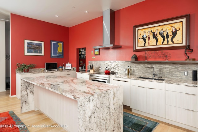 kitchen with white cabinetry, wall chimney range hood, sink, light stone counters, and light hardwood / wood-style flooring