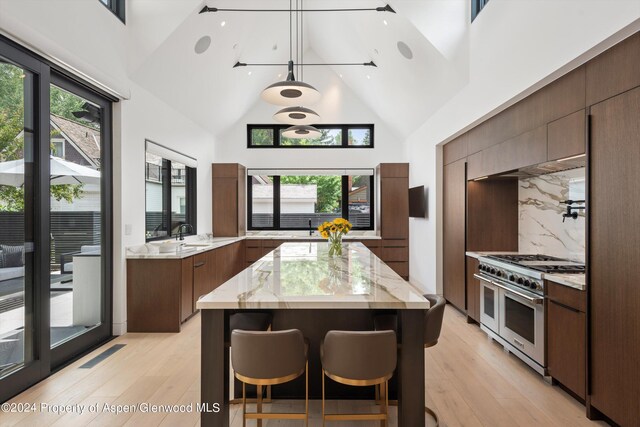 kitchen featuring decorative backsplash, light stone countertops, high vaulted ceiling, range with two ovens, and a center island