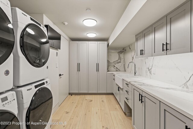 laundry room with cabinets, sink, stacked washing maching and dryer, and light wood-type flooring