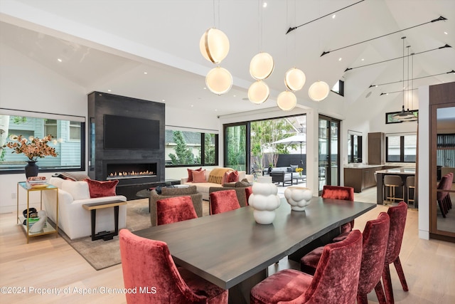 dining space with light hardwood / wood-style floors, a fireplace, and high vaulted ceiling