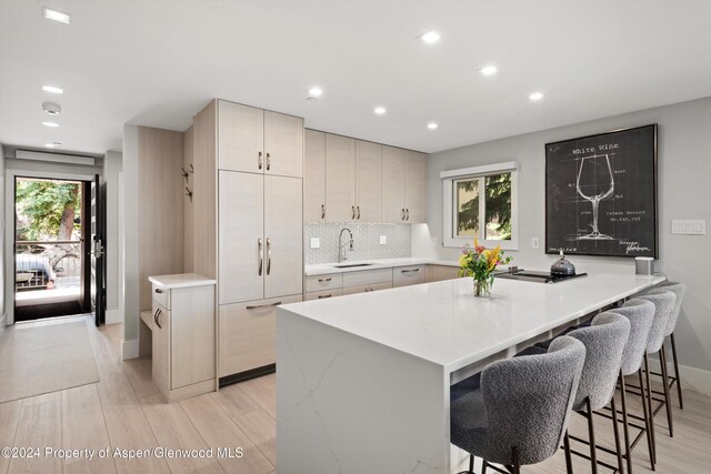 kitchen with sink, a center island, a kitchen bar, decorative backsplash, and light wood-type flooring