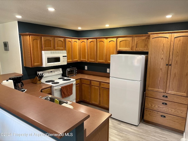 kitchen with white appliances, visible vents, brown cabinets, a peninsula, and light wood-style floors