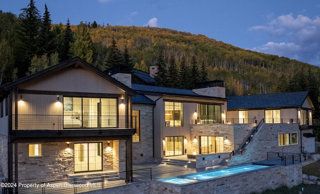 back of property featuring an in ground hot tub, a balcony, a patio, and a mountain view