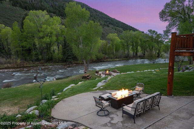2134 Lower River Rd, Snowmass, CO 81654 - patio terrace at dusk with an outdoor fire pit, a yard, a water and mountain view, and a forest view