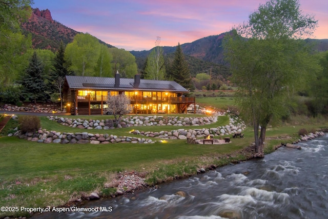 2134 Lower River Rd, Snowmass, CO 81654 - back of house at dusk with a chimney, a yard, a deck with mountain view, metal roof, and a forest view