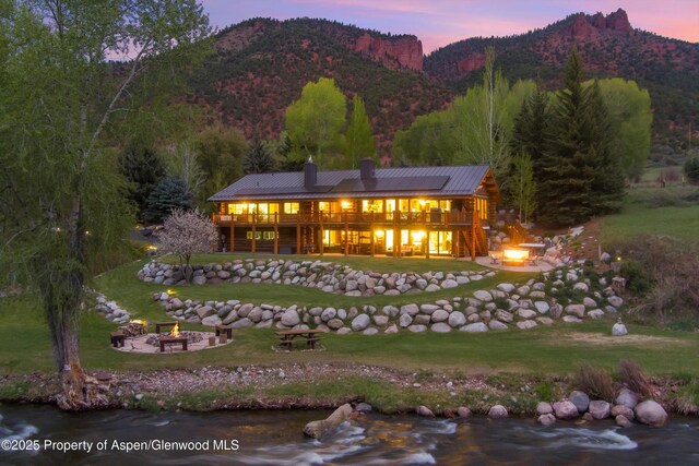 2134 Lower River Rd, Snowmass, CO 81654 - back of house at dusk featuring a fire pit, a chimney, a lawn, and a deck with mountain view
