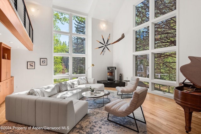 living room featuring a high ceiling, light hardwood / wood-style flooring, a wood stove, and a healthy amount of sunlight