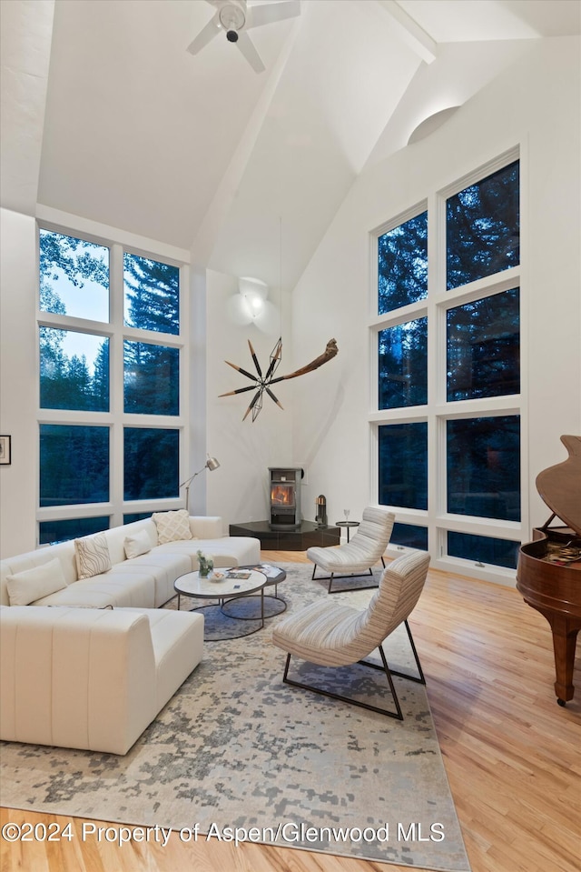 living room with a wood stove, high vaulted ceiling, ceiling fan, beamed ceiling, and light hardwood / wood-style floors